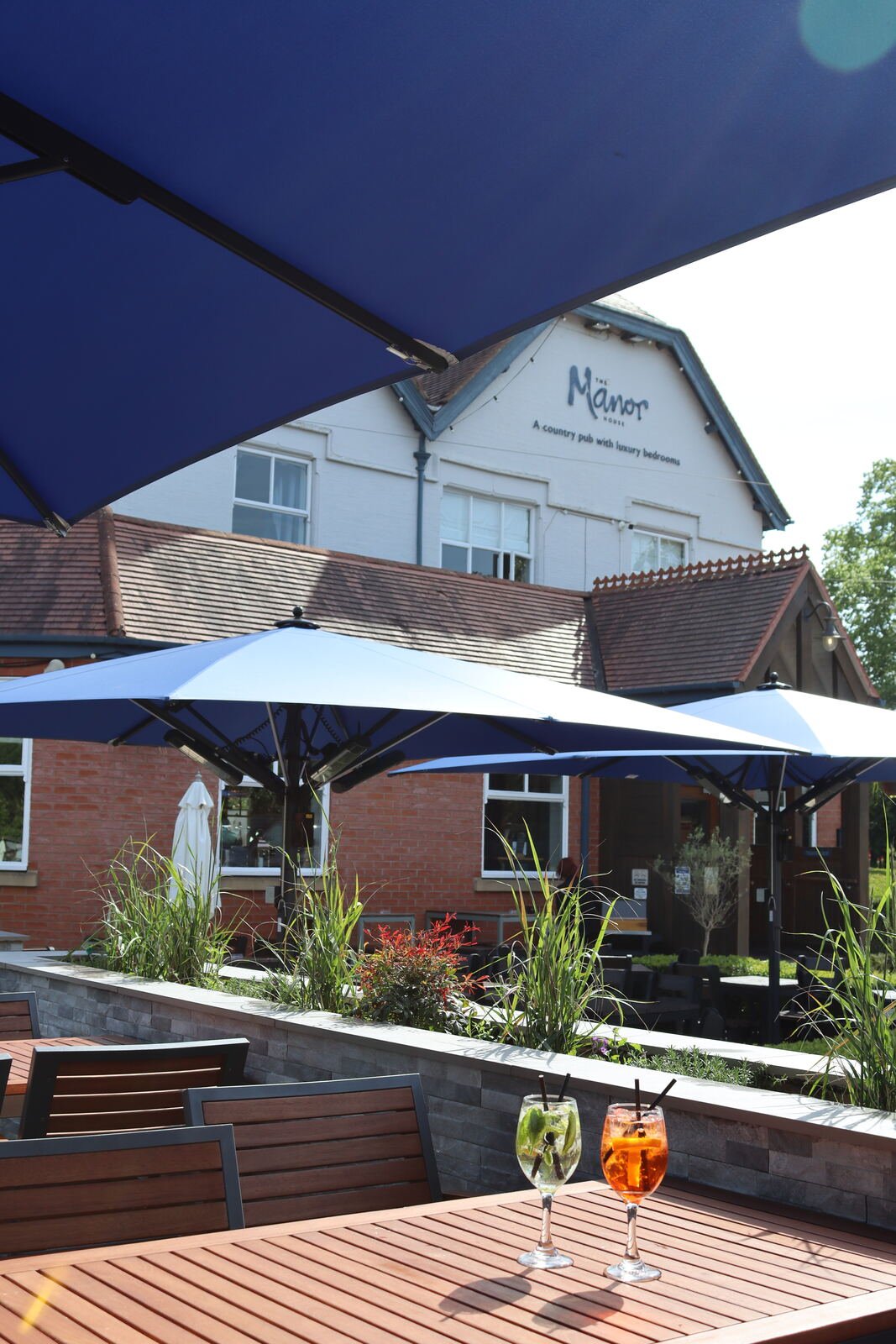 Cocktails on a terrace table shaded by navy parasols, with the building and planted borders behind